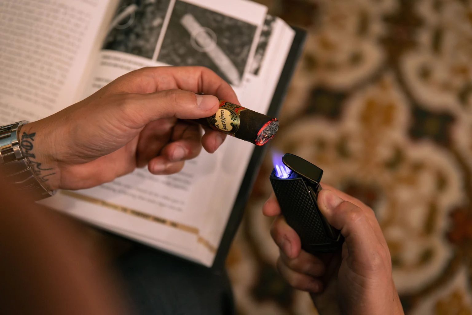 Hands holding a lit Brick House cigar and torch lighter over an open cigar guide