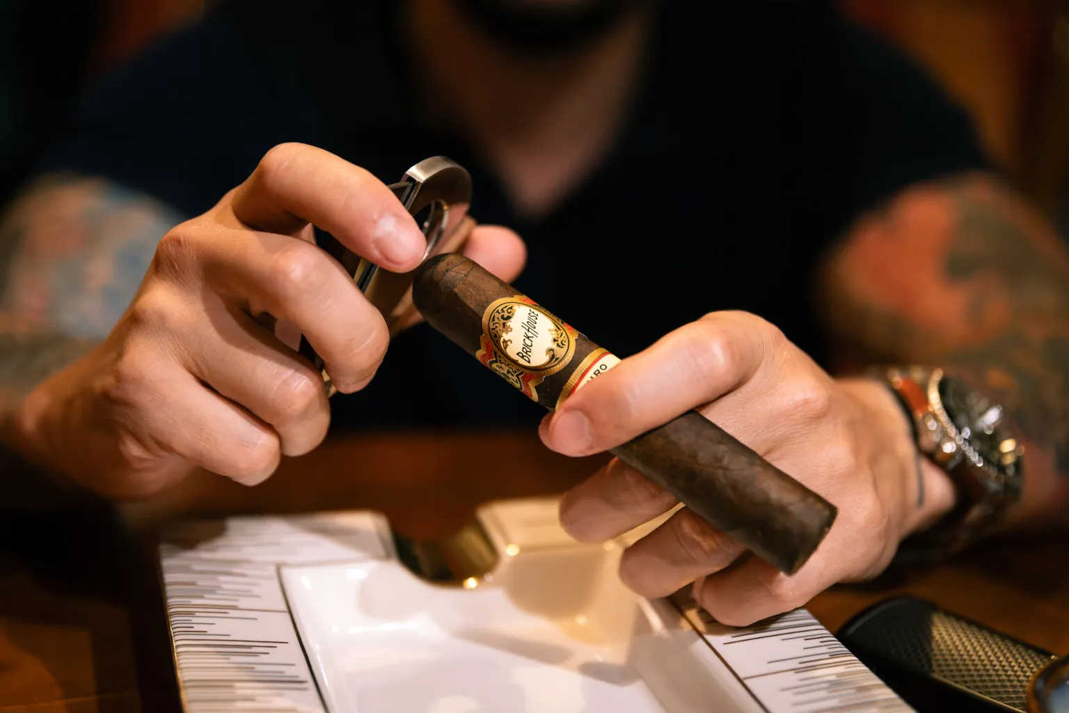 Hands positioning a double-guillotine cutter over the cap of a Brick House cigar