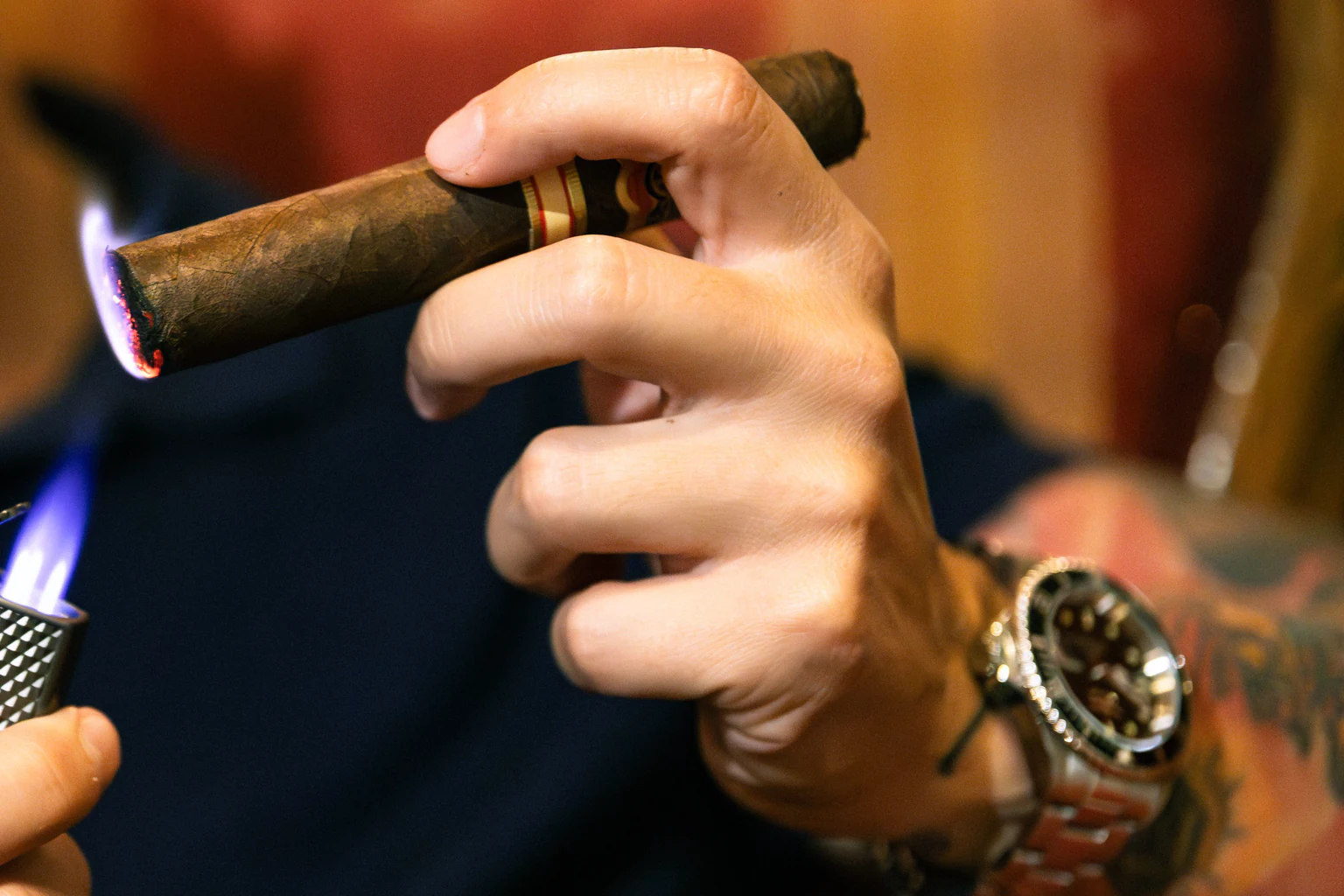 Hands toasting the foot of a cigar above a torch lighter flame
