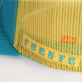 Close up of Fuente embroidered on the yellow mesh of the Opus X Society trucker hat